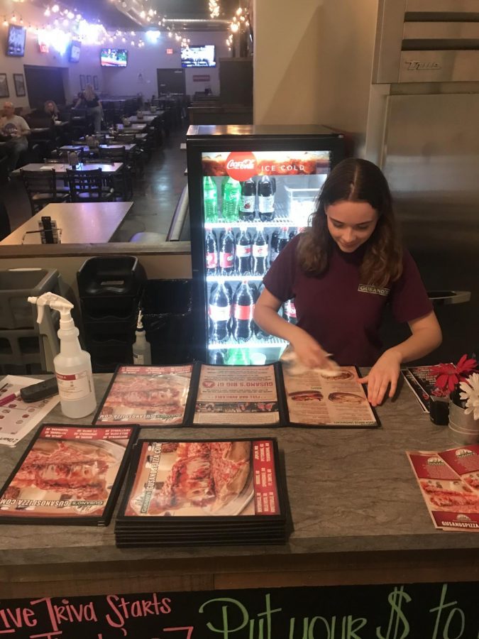 Senior Jaimee Hurless cleans menus at the counter at Gusanos Pizza in Tontitown. The pizza place stayed open during the week of March 16-20. 